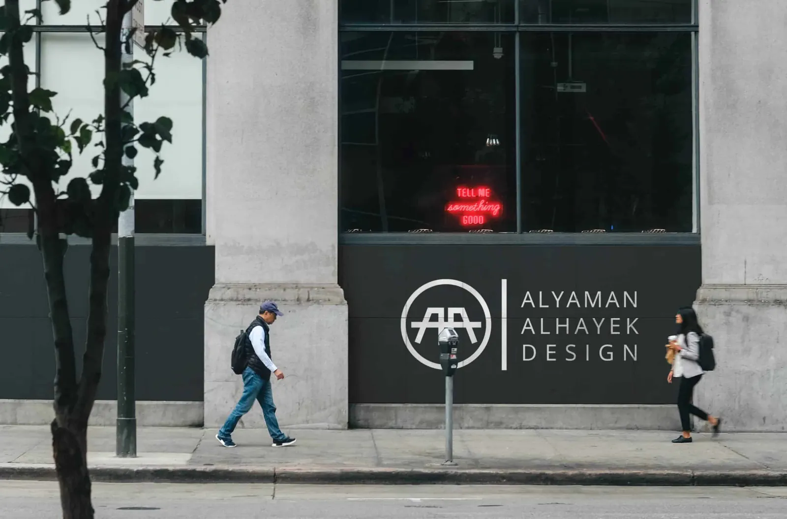 The Alyaman Alhayek Design logo on a storefront wall as people walk past.