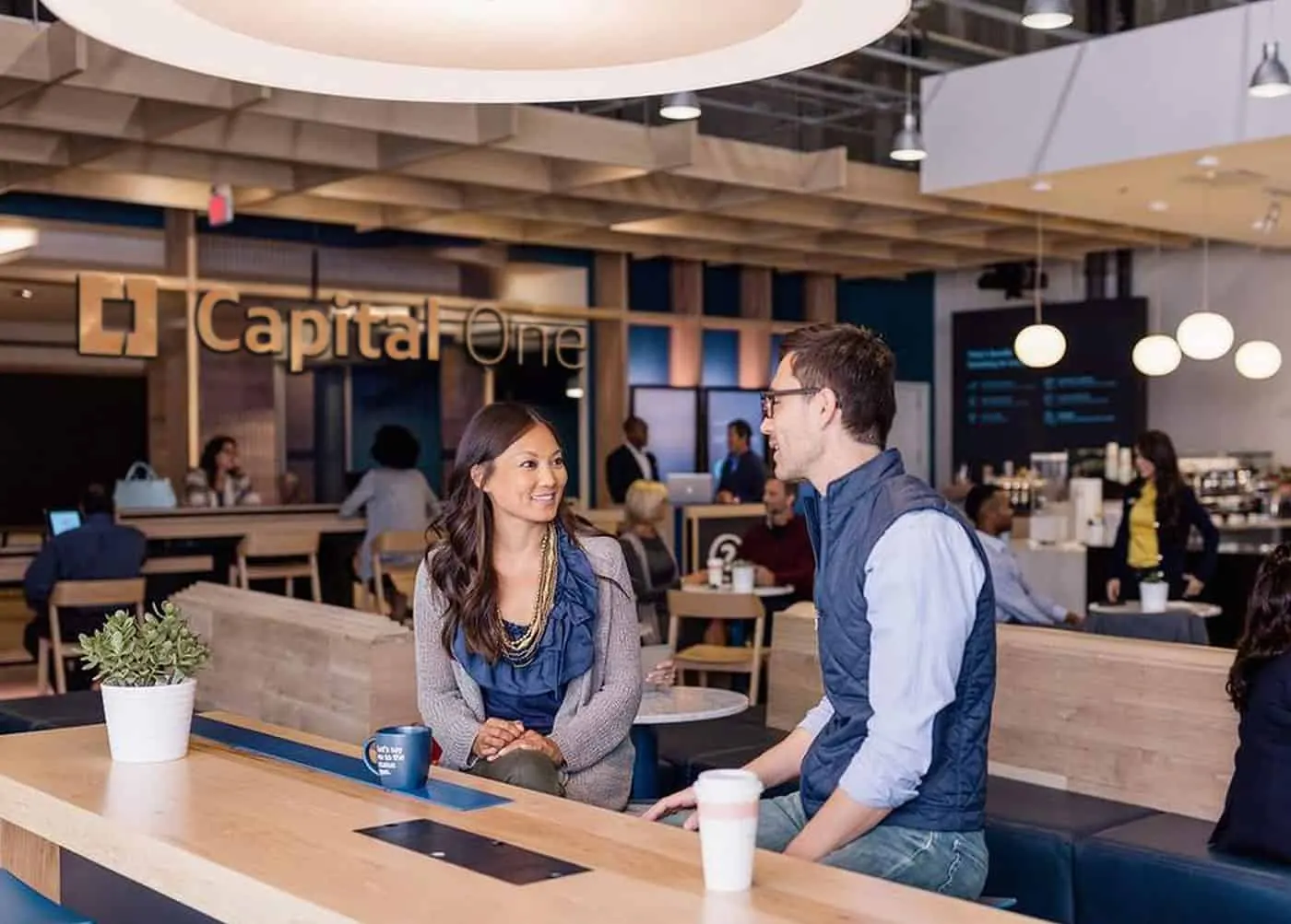 A smiling staff member talks with a customer inside a Capital One cafe.