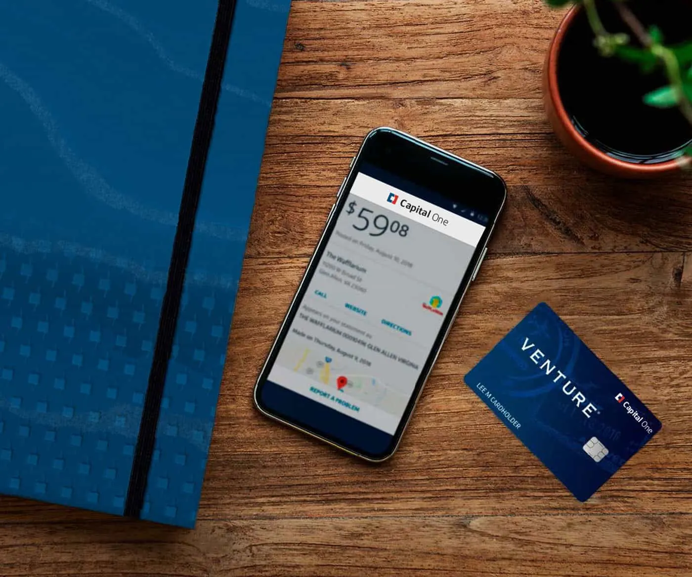 A phone showing a banking app beside a Capital One card on a desk.