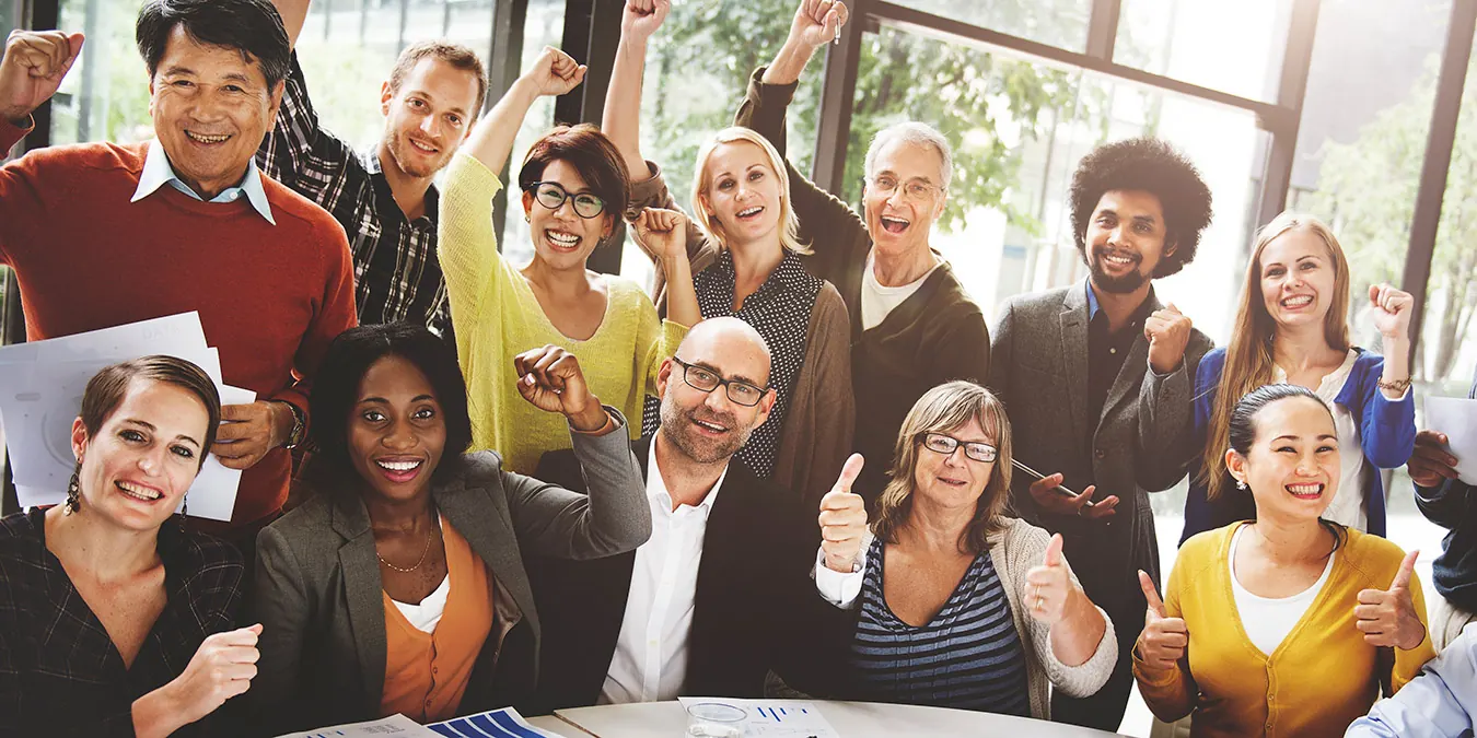 A large business team cheers with arms raised in an office.