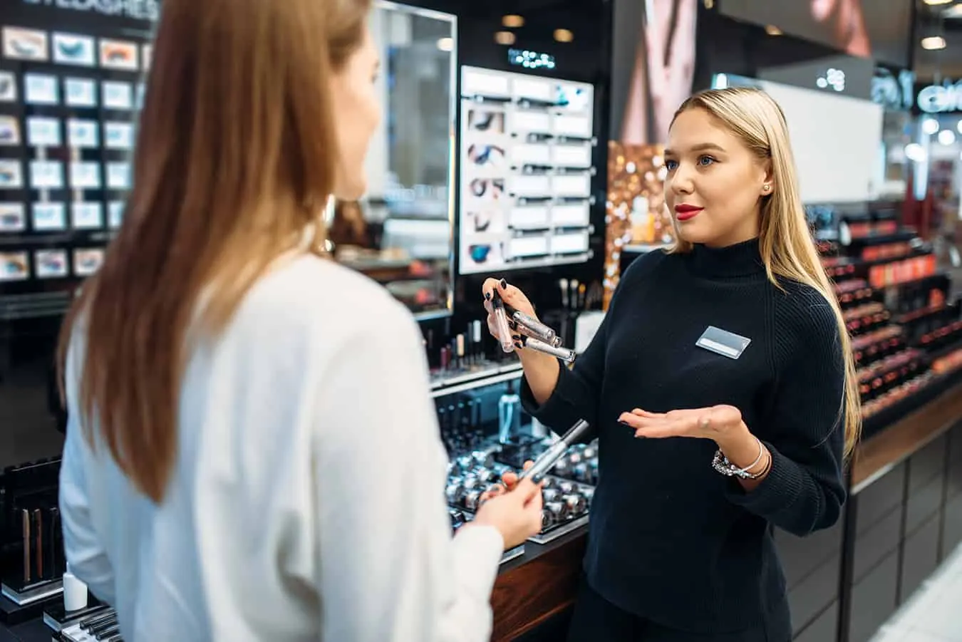 A cosmetics consultant shows products to a customer in a beauty store.