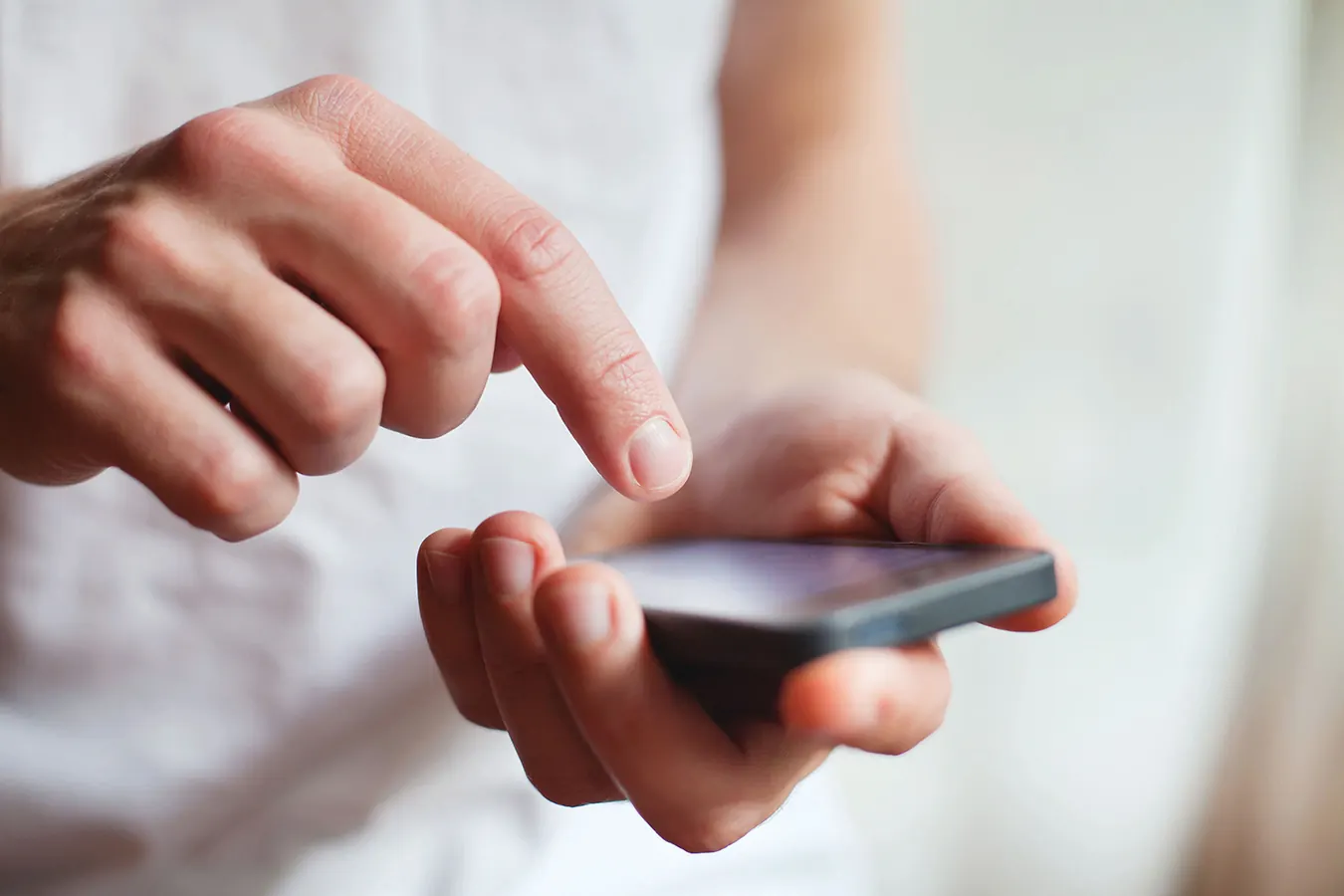 A finger touches a smartphone screen held in the other hand.