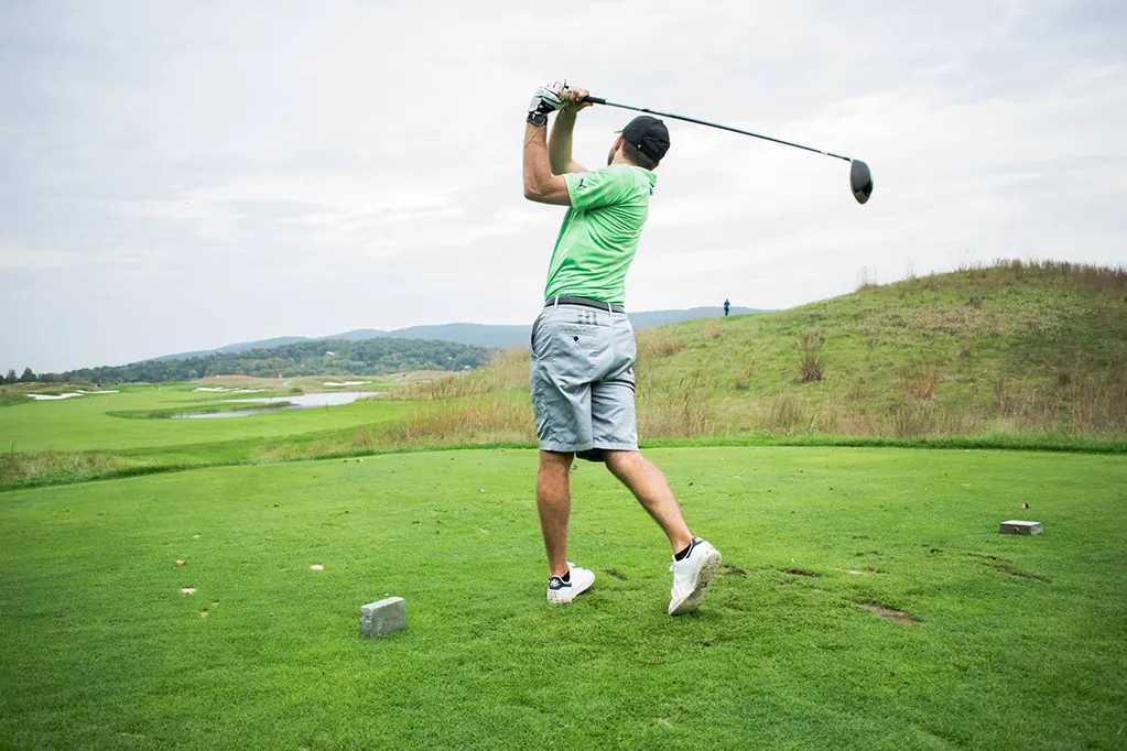 A golfer in a green shirt swings a driver on a grassy course.