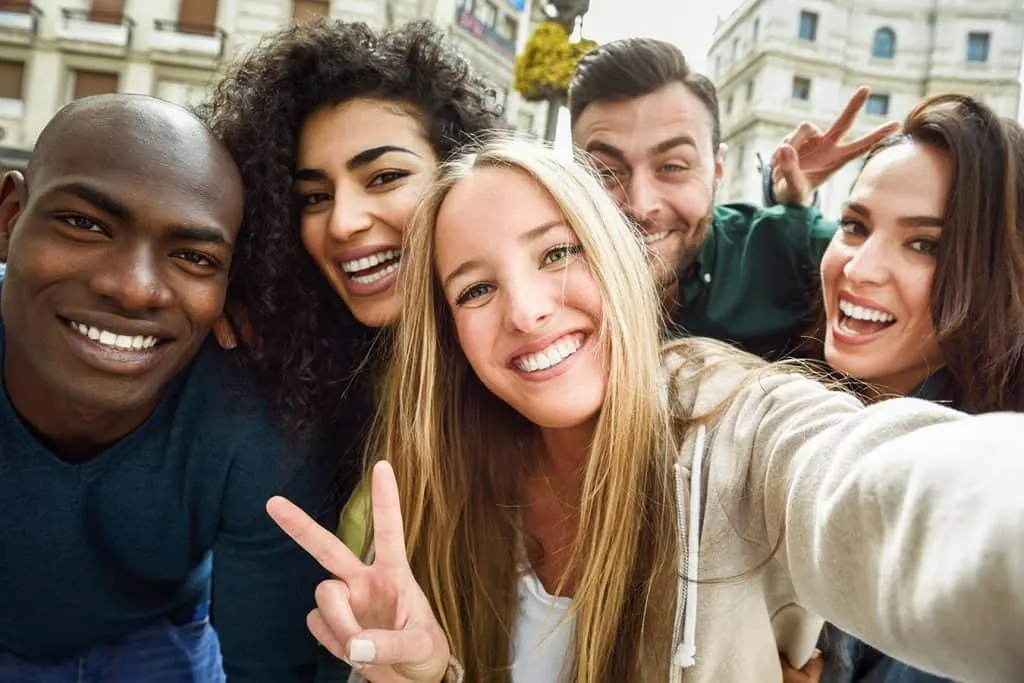A diverse group of smiling friends take a selfie on a city street.