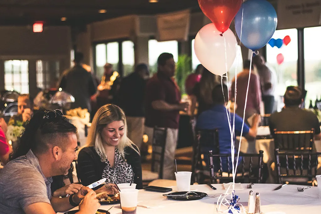 Guests eat and talk at a golf outing dinner with balloons.