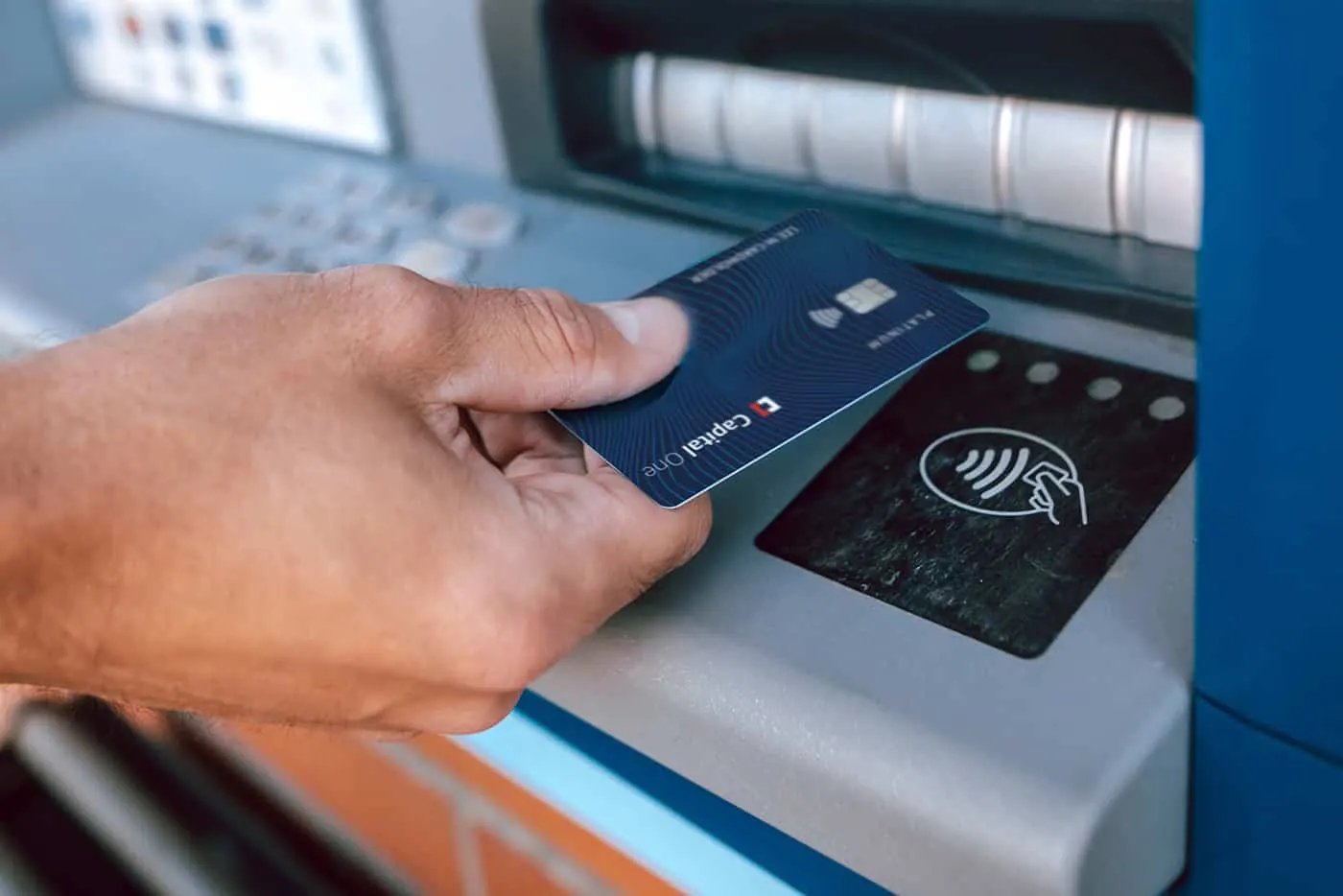 A hand taps a Capital One card on a contactless payment reader.