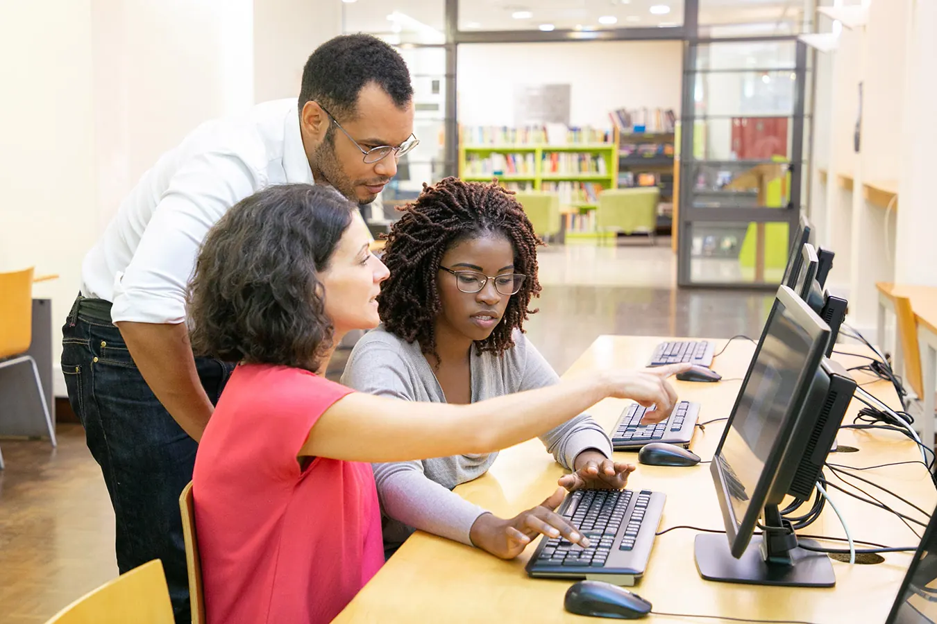 An instructor helps two students working at computers in a classroom.
