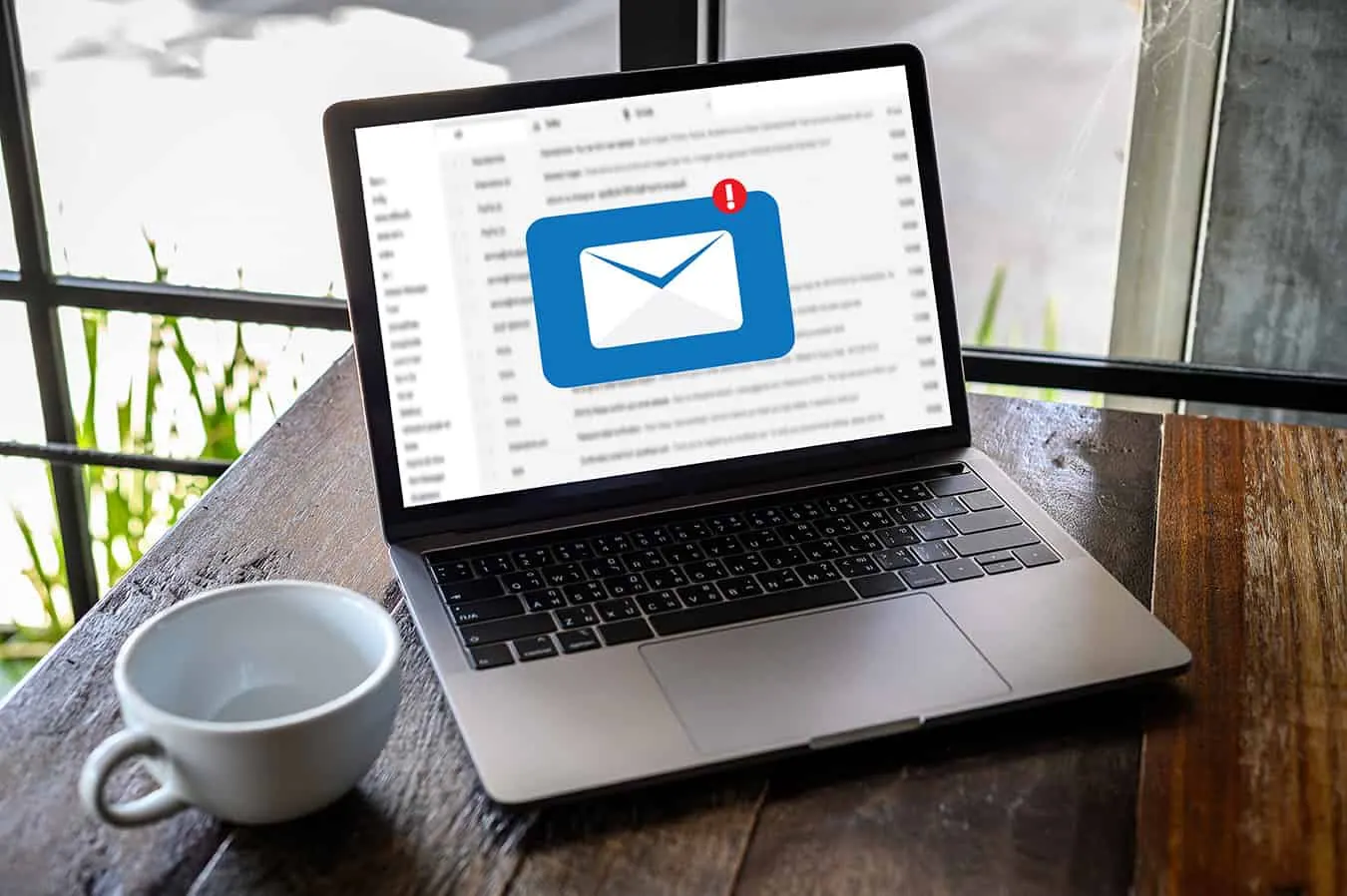 A laptop on a wooden table shows a new email notification icon.