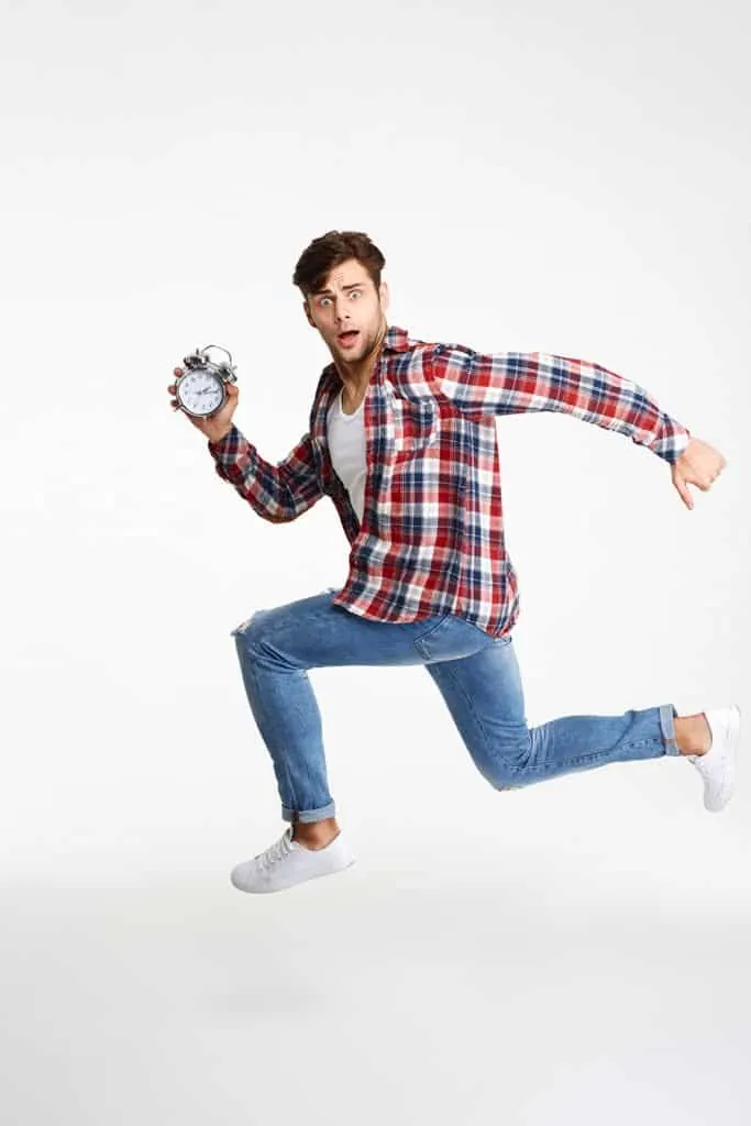 A young man in a plaid shirt runs while holding an alarm clock.