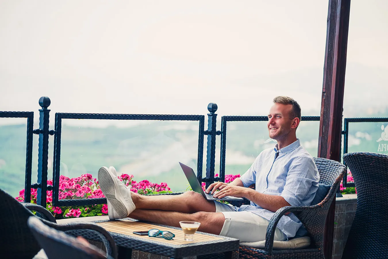 A man works on a laptop with his feet up on a seaside balcony.