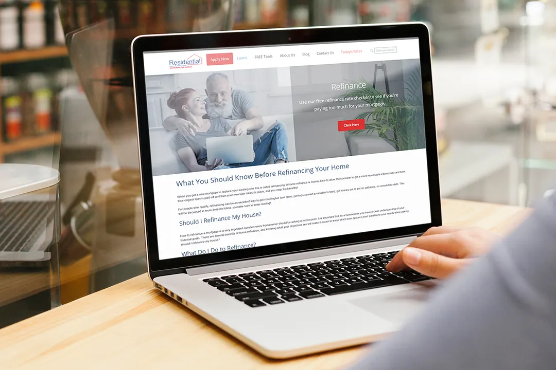 A laptop on a wooden table showing a Residential Home Funding refinance page.