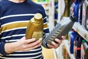 A shopper holds two motor oil bottles side by side to compare brands.