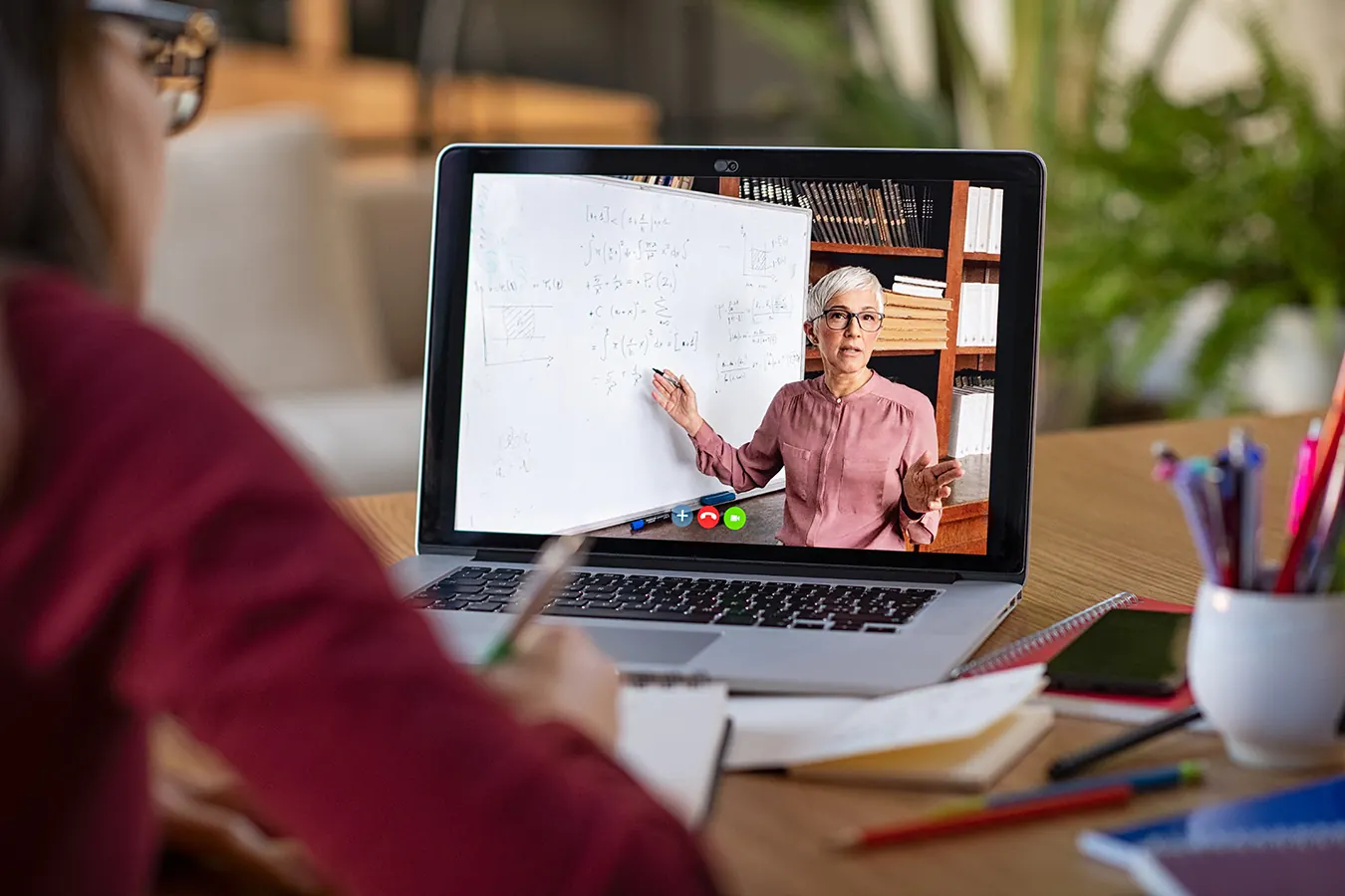 A student watches a teacher give an online lesson on a laptop.