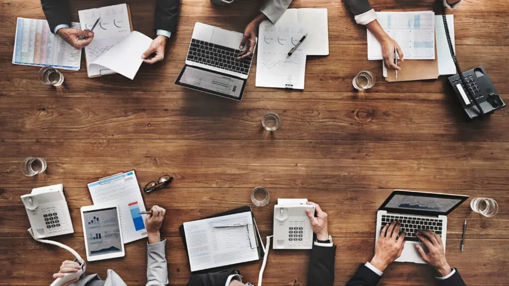 Overhead view of a team working with laptops and papers at a wooden table.