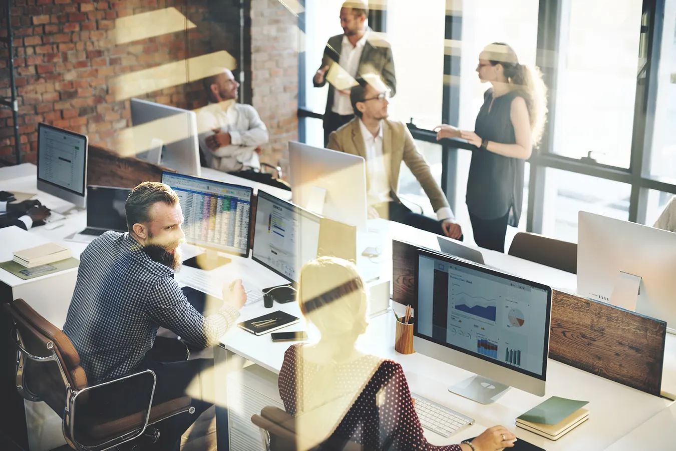 A team works at computers and talks in a bright open office.