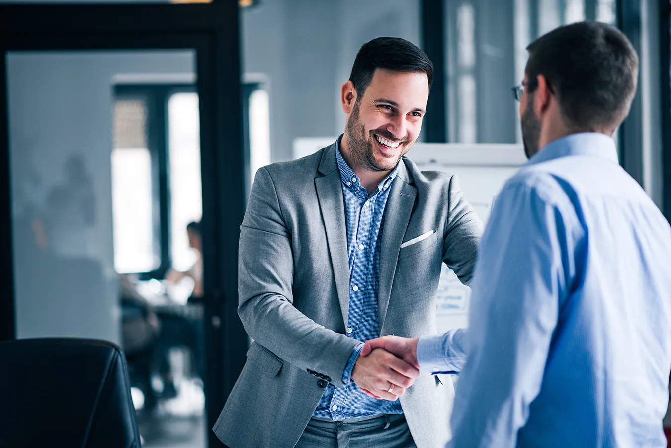 Two smiling businessmen shake hands in a bright modern office.