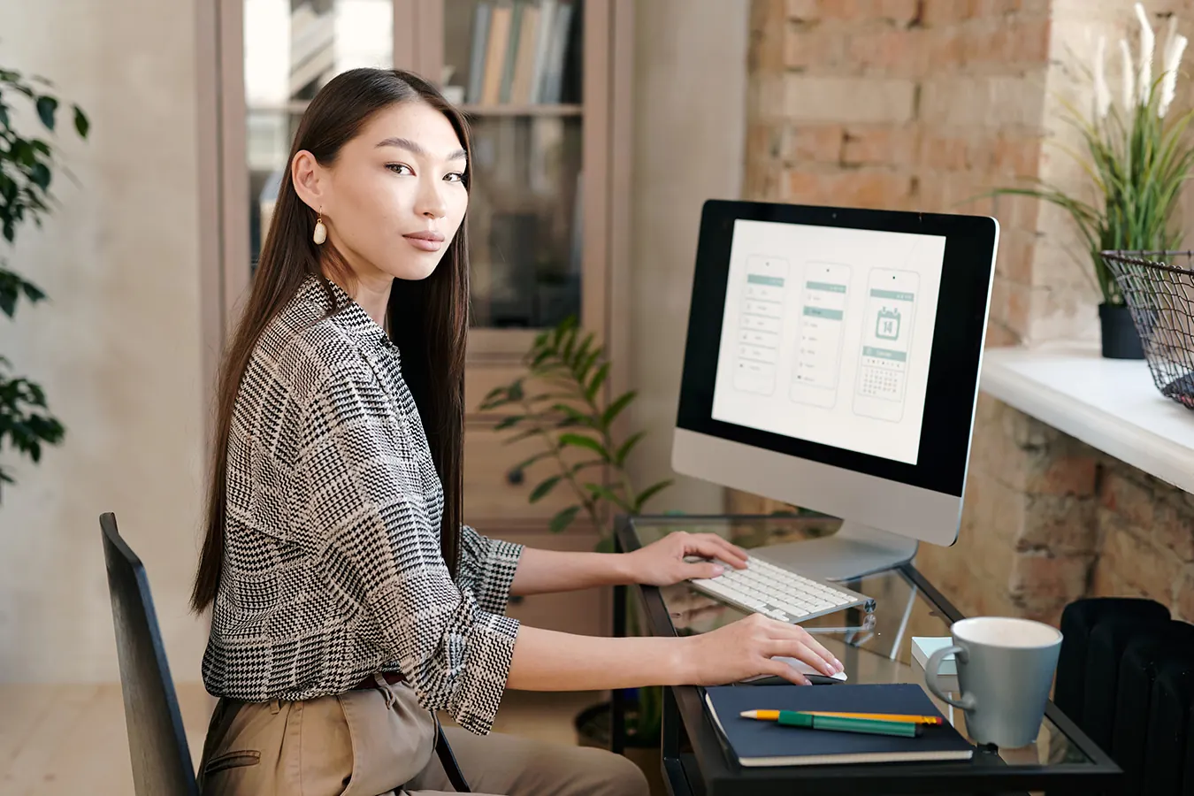 A woman works on a design at a desktop computer in a bright office.