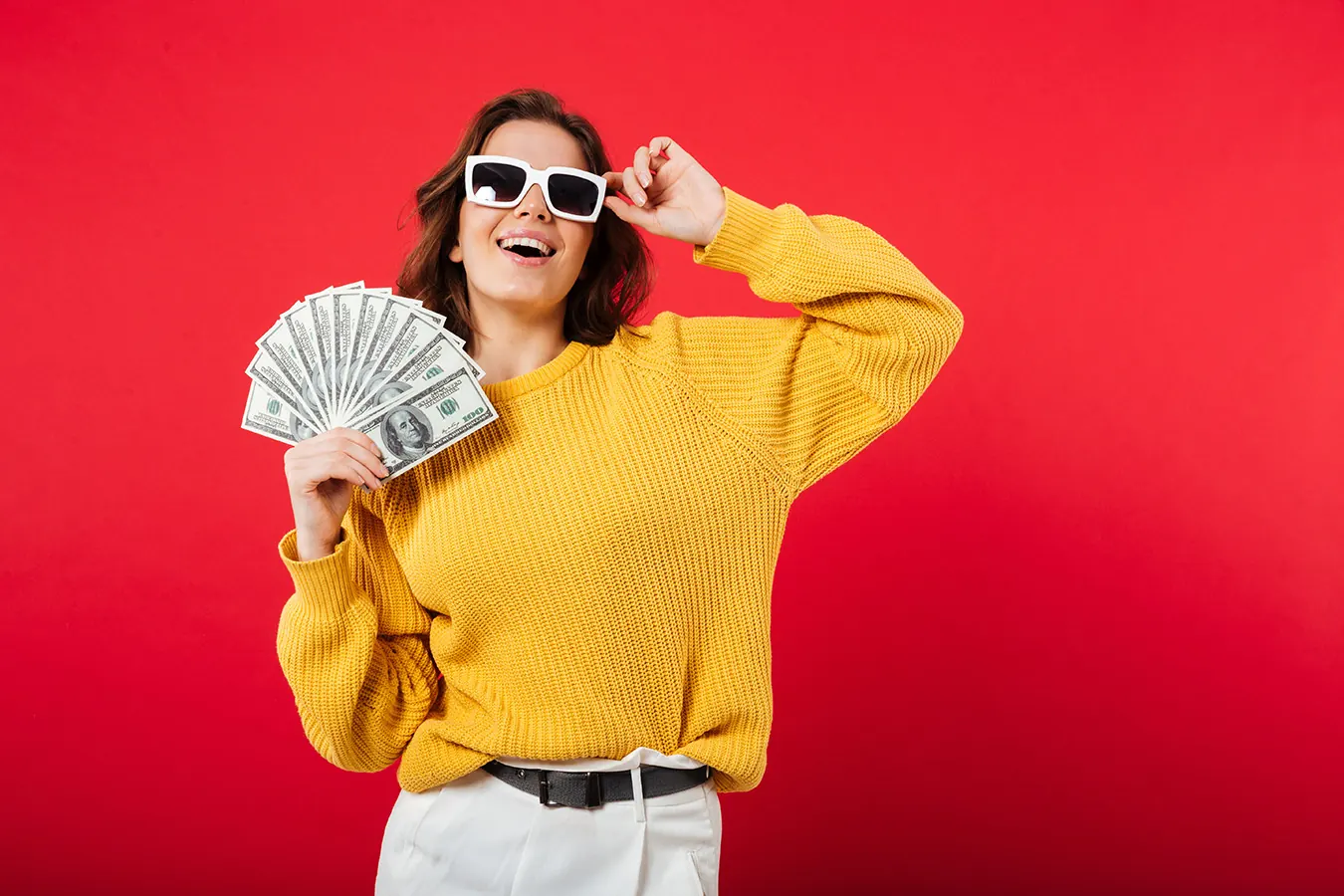 A smiling woman in sunglasses and a yellow sweater fans out cash.