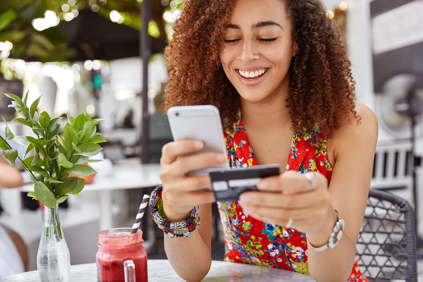 A smiling woman shops on her phone while holding a credit card.