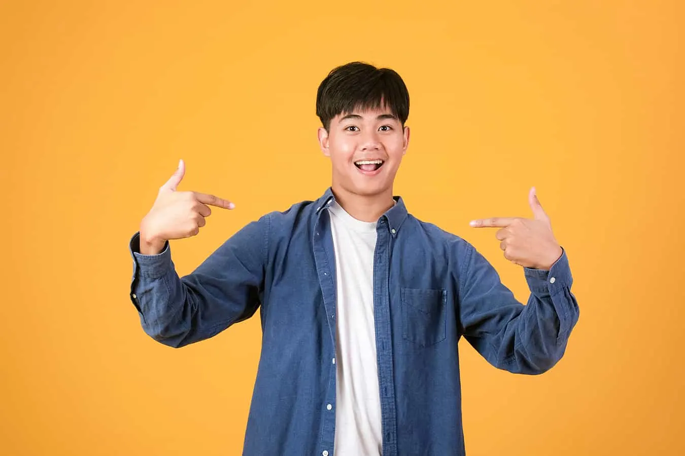 A smiling young man points at himself against a bright yellow background.