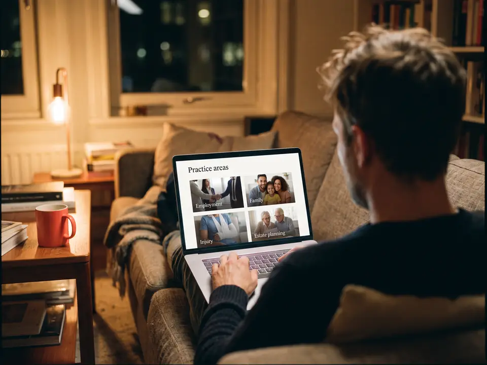 A man on his couch at night browses a law firm's practice areas page on his laptop.