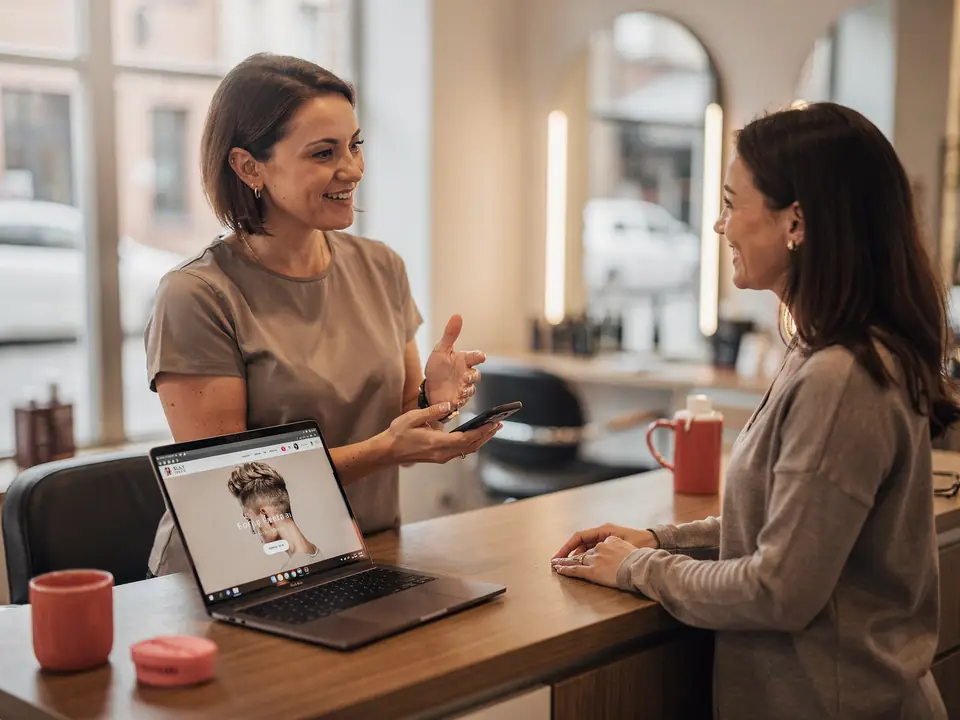 A hair salon owner shows a client her new website on her phone.