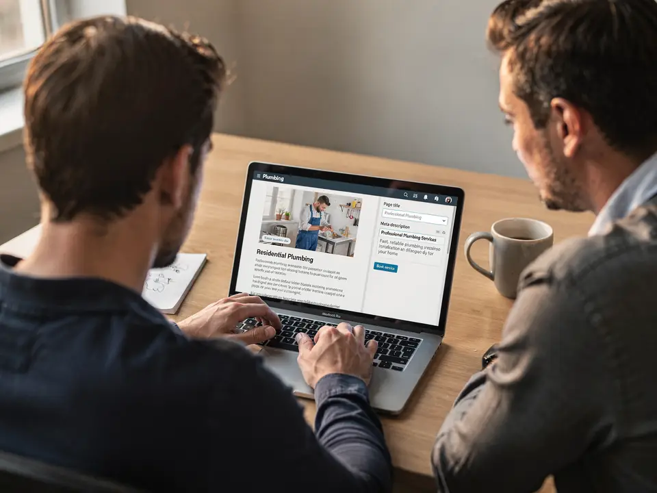 A web specialist edits a plumbing page title and meta description on a laptop.