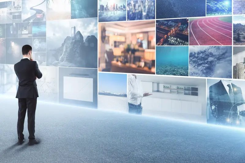 A businessman in a suit stands facing a large wall of stock photos.