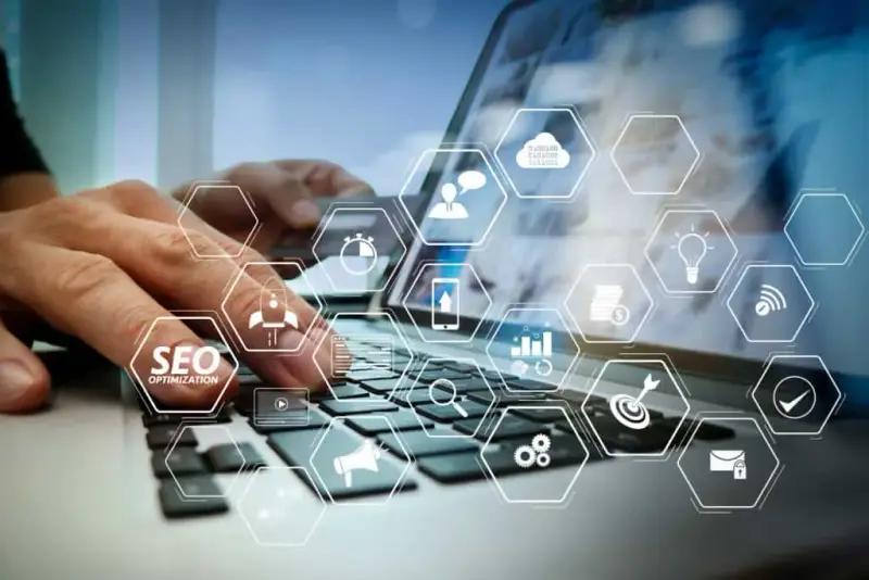 Hands typing on a laptop keyboard with floating SEO and web icons.