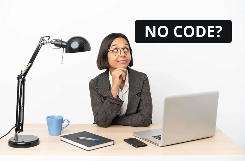 A woman in glasses sits at a laptop under a No Code sign.